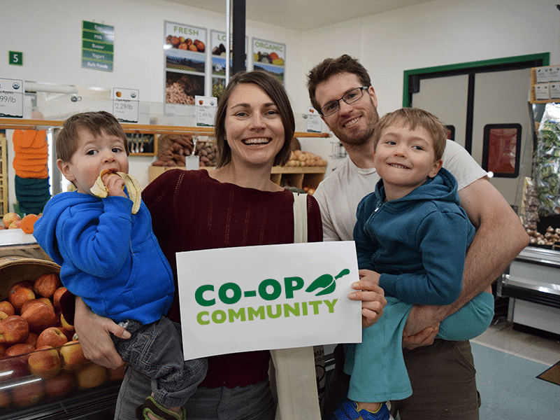 Young family of four stand in the store holding a sign saying "Co-op Community"