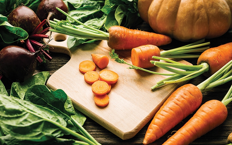 carrots, beets, spinach, pumpkin on a wooden background, cutting board and knife, fresh vegetables